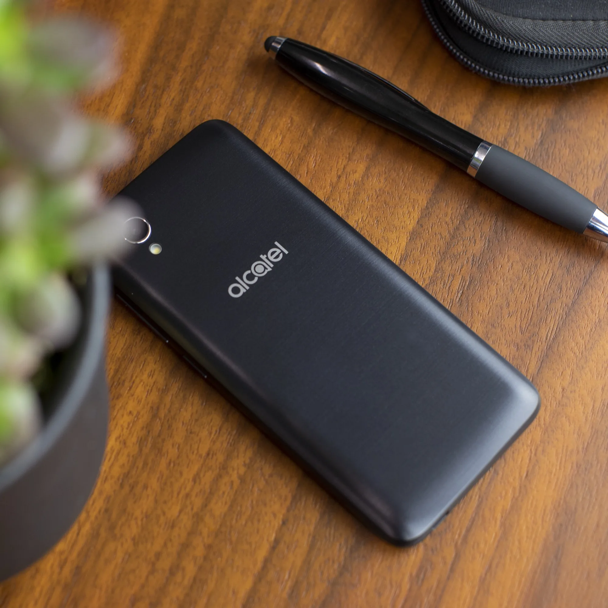 Black Alcatel handset on a walnut desk beside a pen